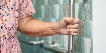 Elderly woman using grab rails in bathroom.