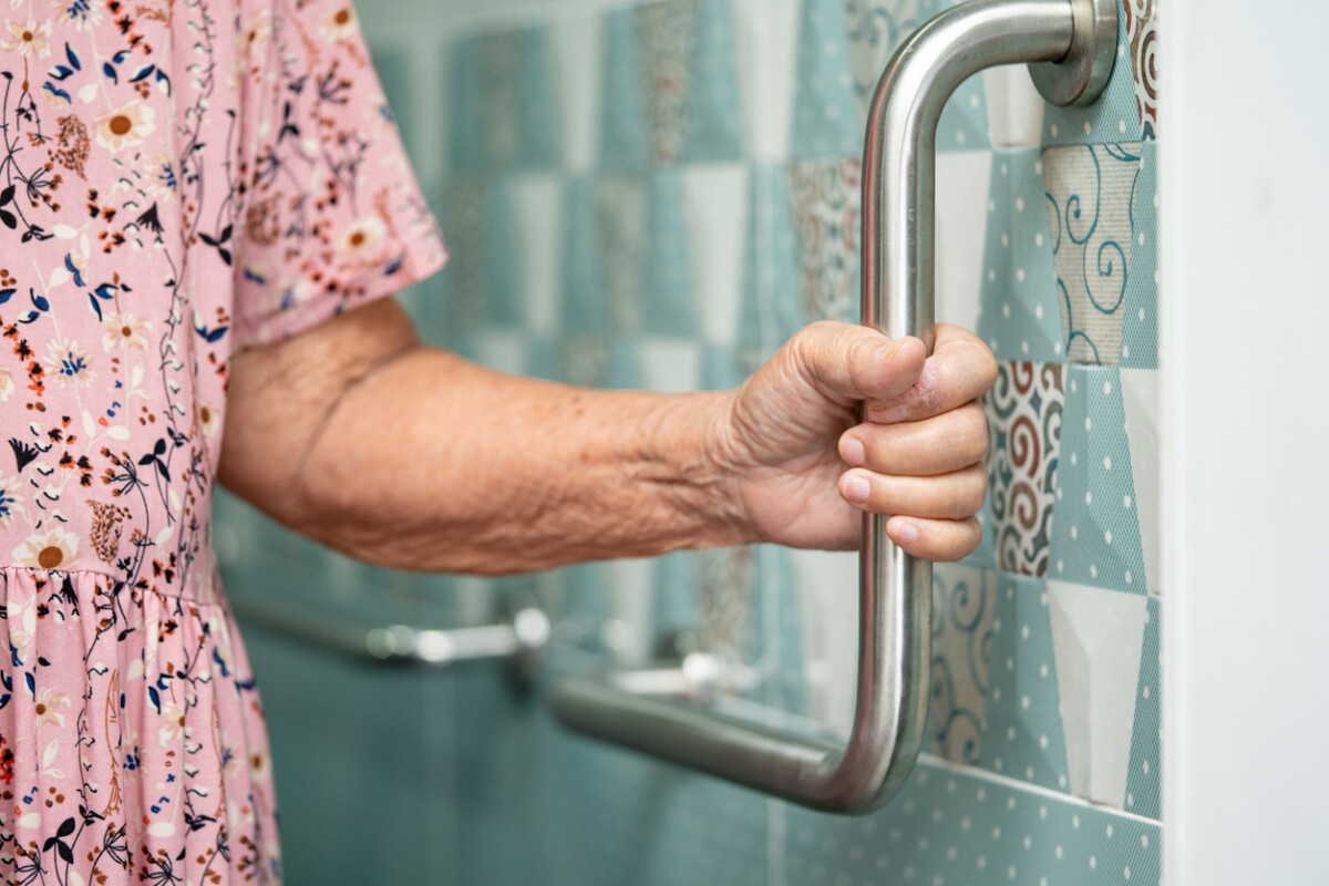 Elderly woman using grab rails in bathroom.