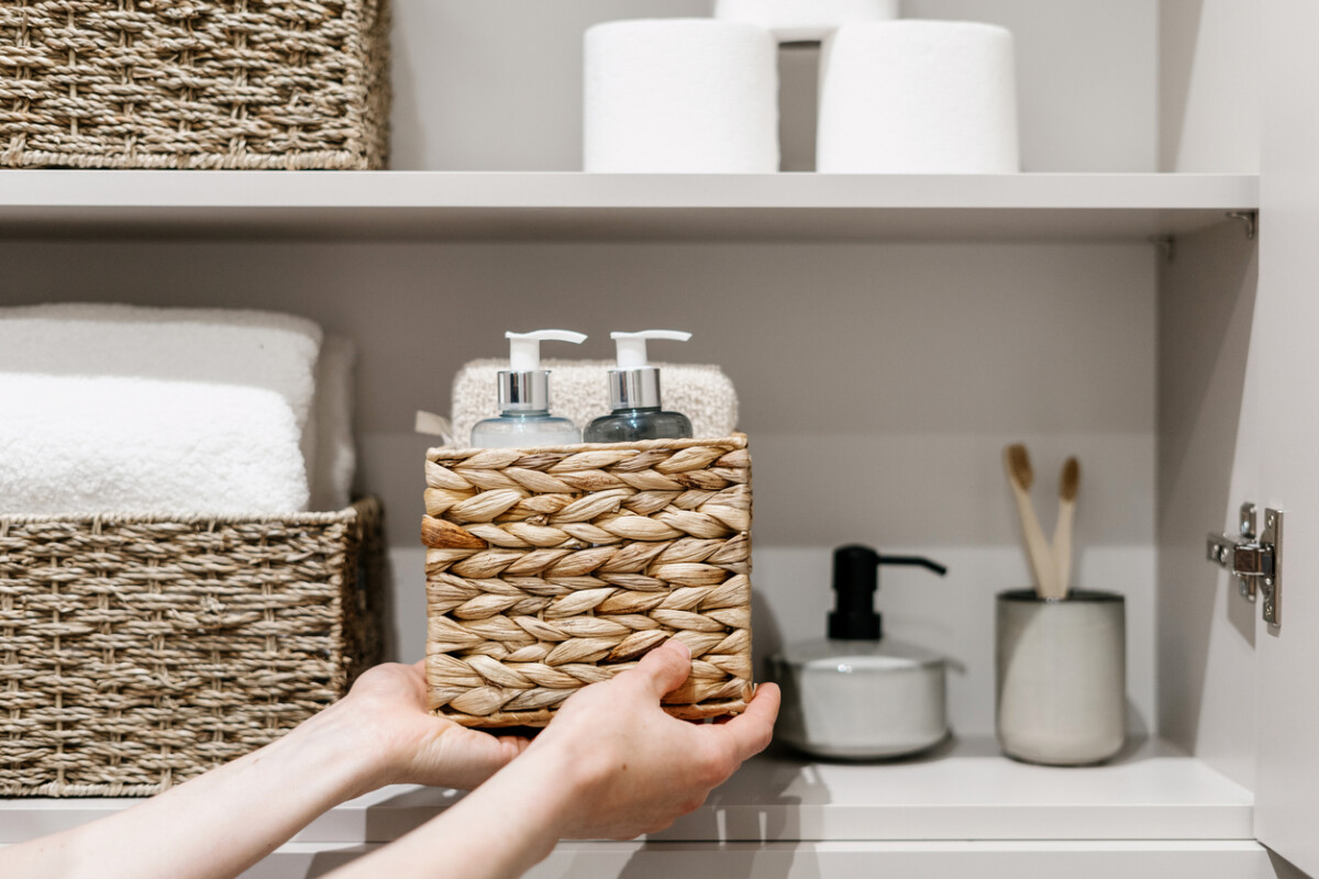 Woman puts wicker box with cosmetics products in bathroom closet