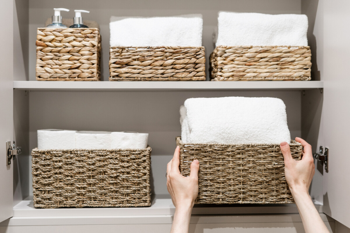 Woman placing spare towels in a bathroom closet with neatly organised shelves.