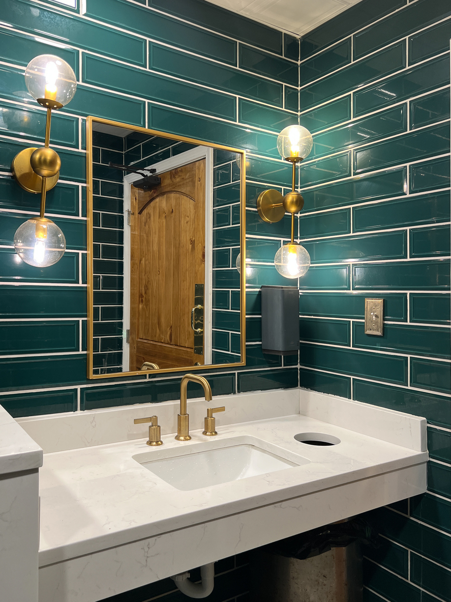 Bathroom with green subway tile walls, featuring a modern sink and minimalist decor.