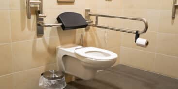 High-level toilet with a handrail, designed for disabled accessibility, in a clean bathroom setting.