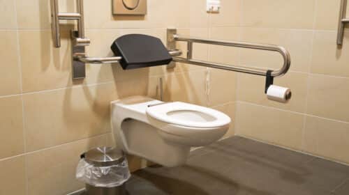 High-level toilet with a handrail, designed for disabled accessibility, in a clean bathroom setting.