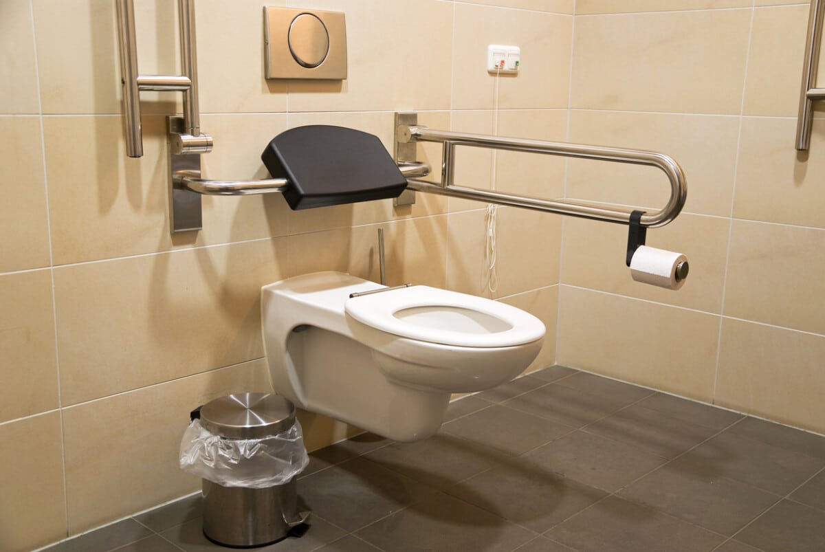 High-level toilet with a handrail, designed for disabled accessibility, in a clean bathroom setting.